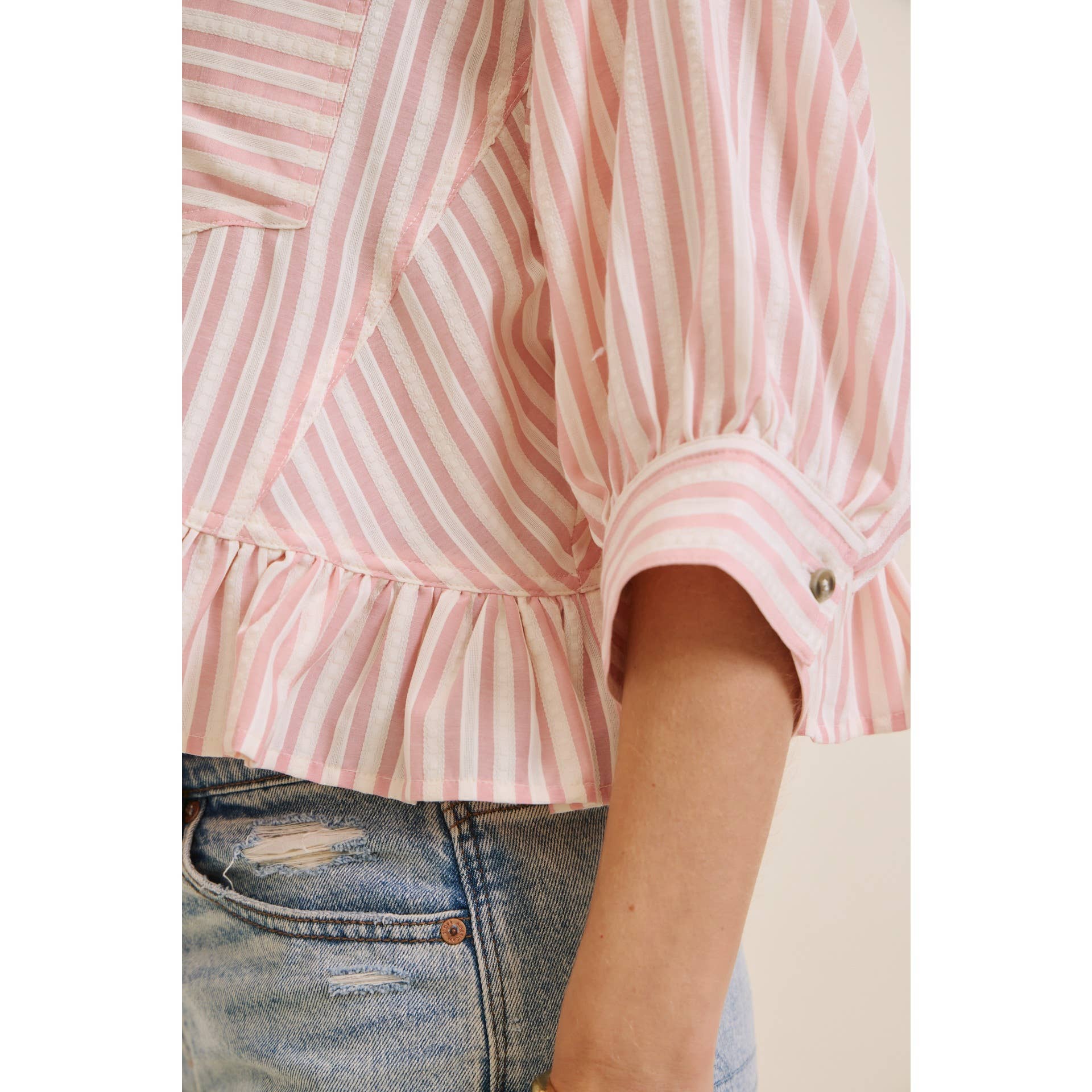 Pink and white striped shirt worn with blue jeans on a plain background