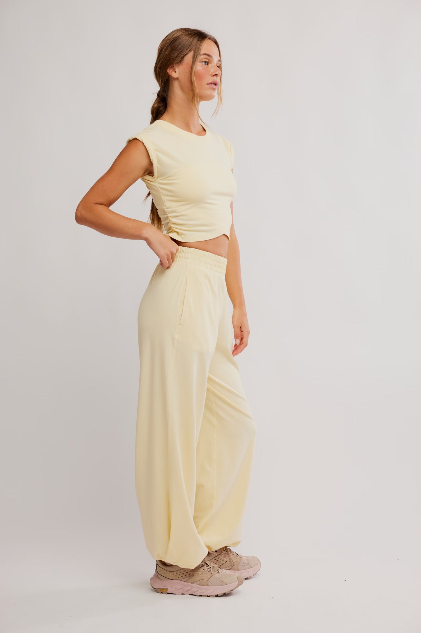 Woman wearing a light yellow sleeveless top and wide-leg pants on a white background