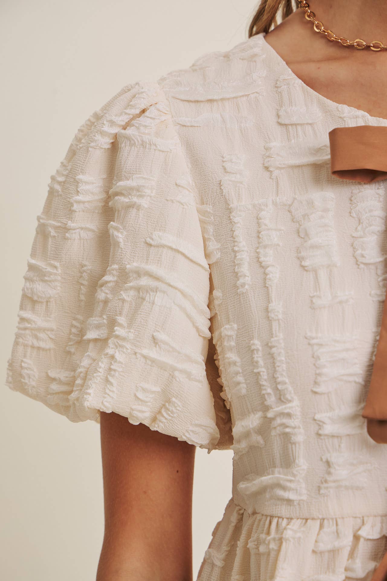 Close-up of a textured white blouse with ruffled sleeves on a neutral background