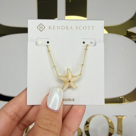 Hand holding a Kendra Scott necklace on a branded card with a decorative background.