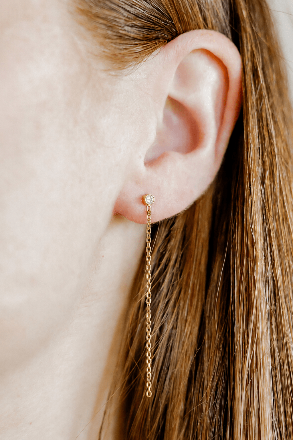 Gold chain earring worn by a person with long hair.