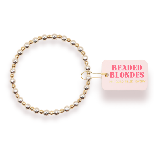 A beaded stretch bracelet with alternating gold and silver-toned beads, shown with a pink tag that reads 'BEADED BLONDES' on a white background.