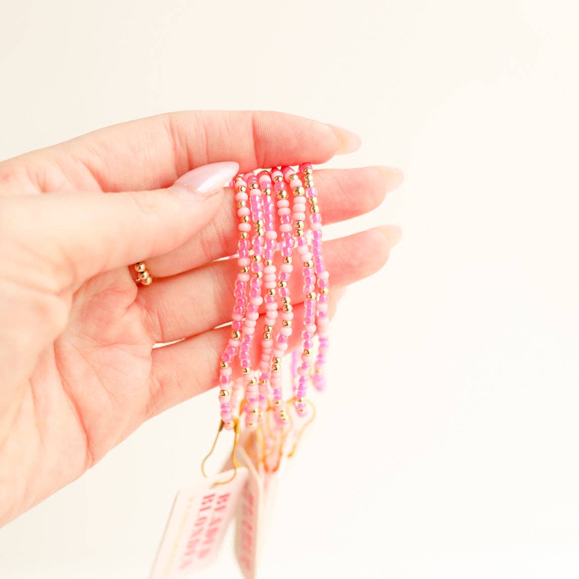 Hand holding beaded bracelets with pink and gold beads on a light background