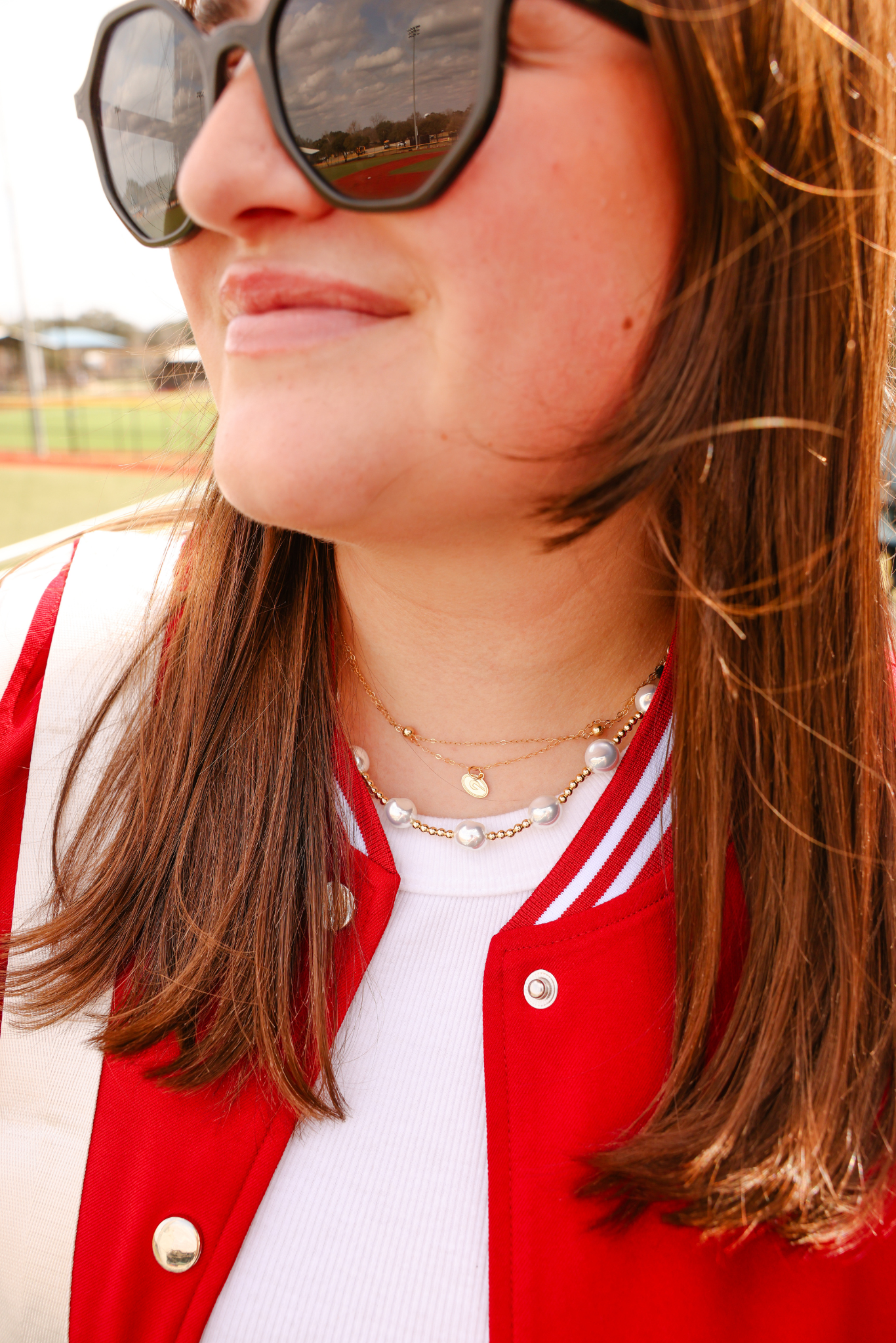 Person wearing a red jacket and sunglasses with a sports field background