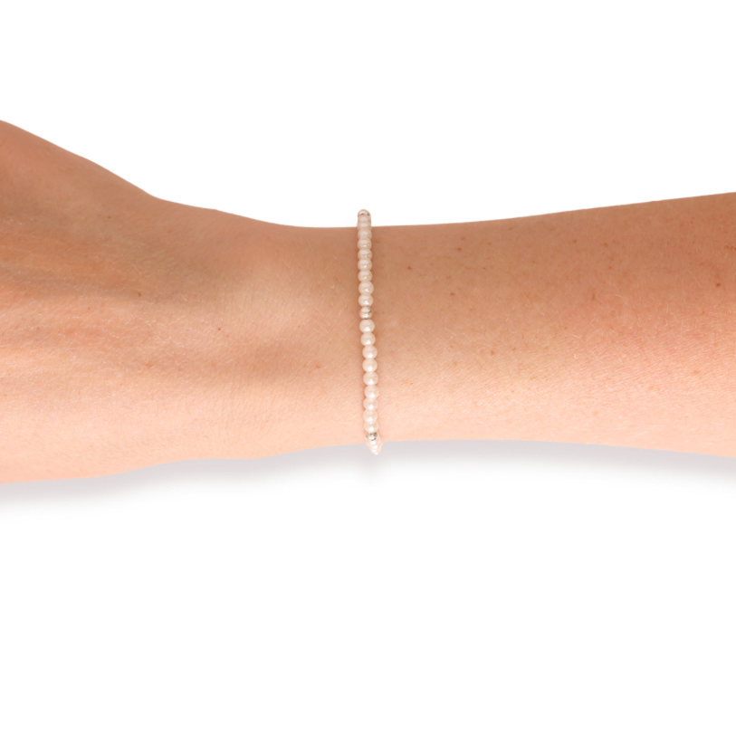 A delicate single-strand pearl bracelet with a silver-toned setting, shown worn on a person's wrist against a plain white background.