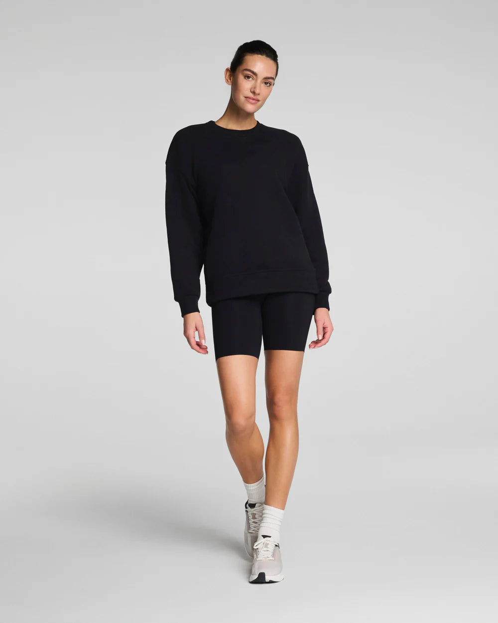 Model wearing black SPANX® BoostUp Cotton Fleece Crewneck Tunic with white background. 