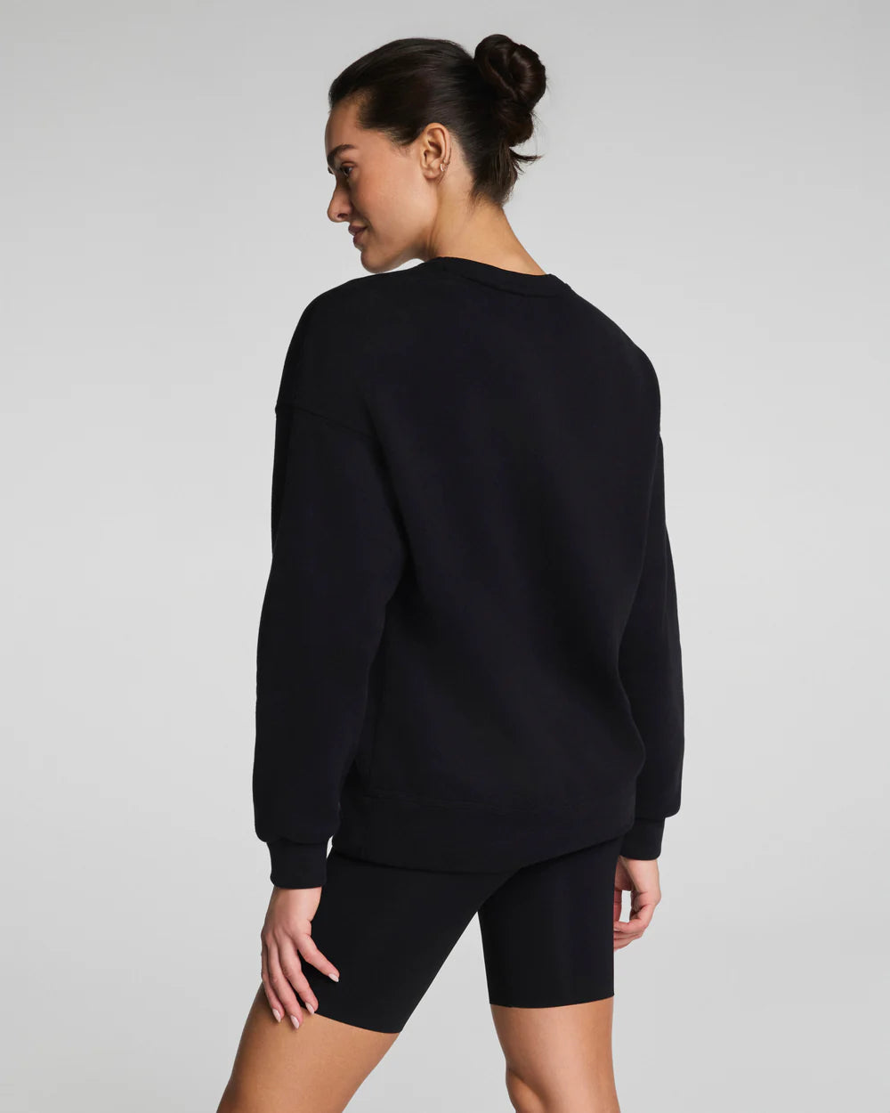 Model wearing a black SPANX® BoostUp Cotton Fleece Crewneck Tunic with white background.