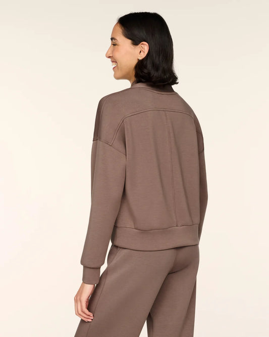 A woman shown from the back wearing a matching taupe-brown cropped sweatshirt and sweatpants set against a plain light beige studio background.