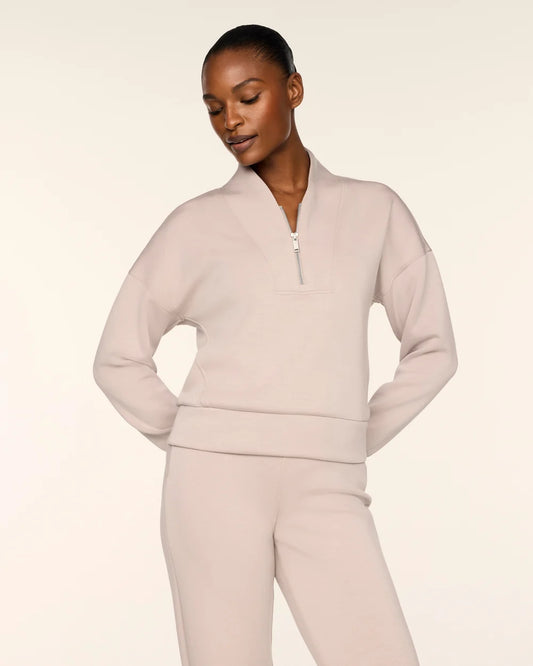 A model wearing a light beige matching lounge set consisting of a cropped quarter-zip sweatshirt and matching sweatpants, photographed against a solid off-white studio background.