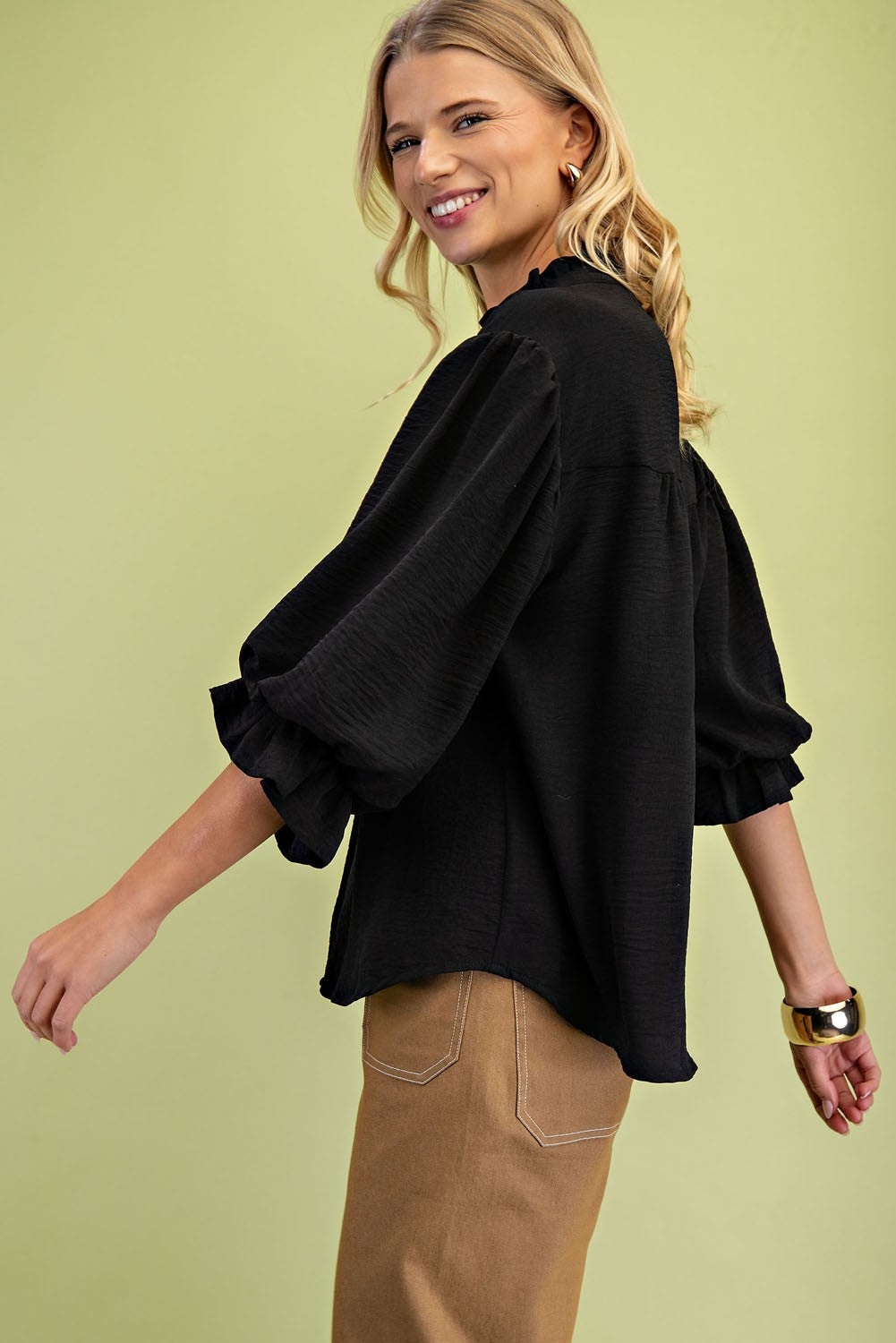 Woman wearing a black blouse with puffed sleeves against a light green background