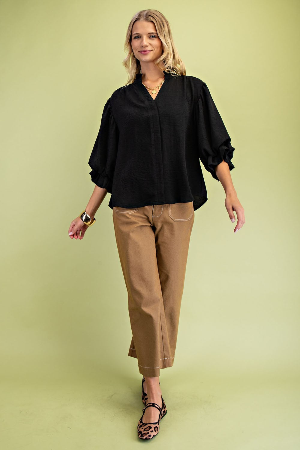 Woman wearing a black blouse and brown pants against a light green background
