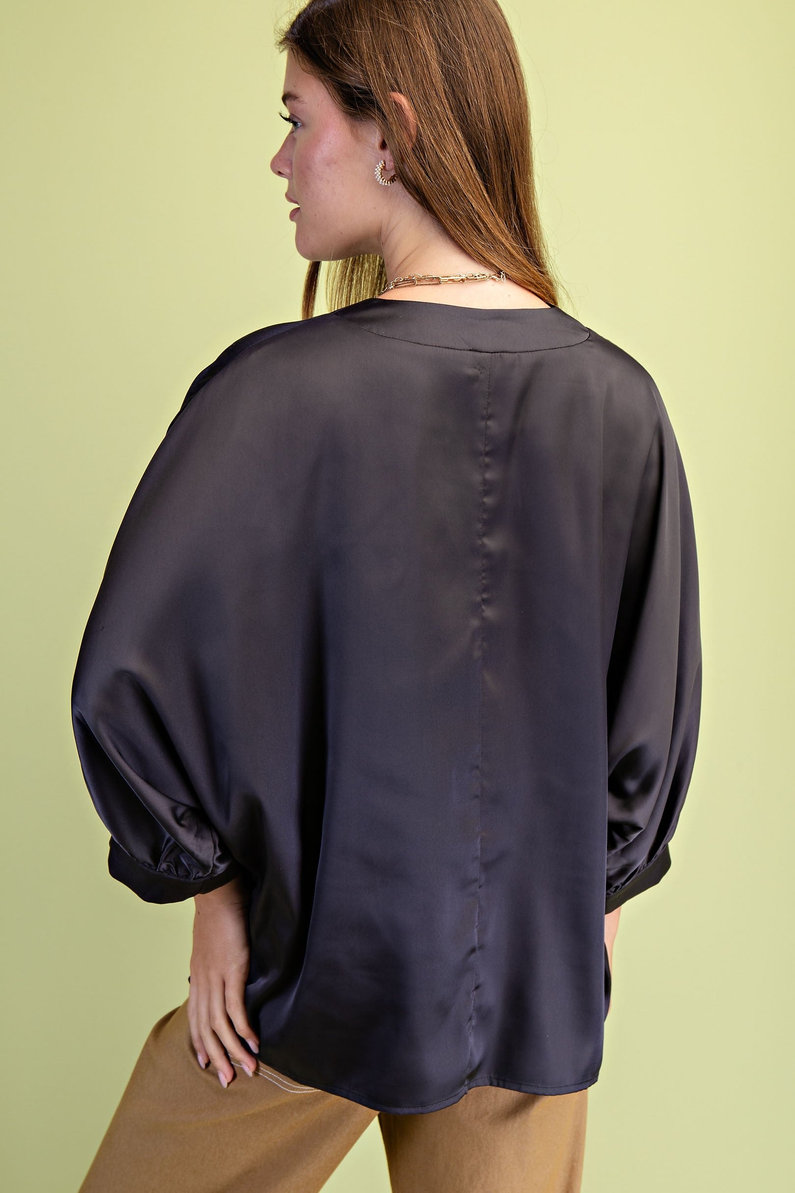 Woman wearing a dark satin blouse against a light green background