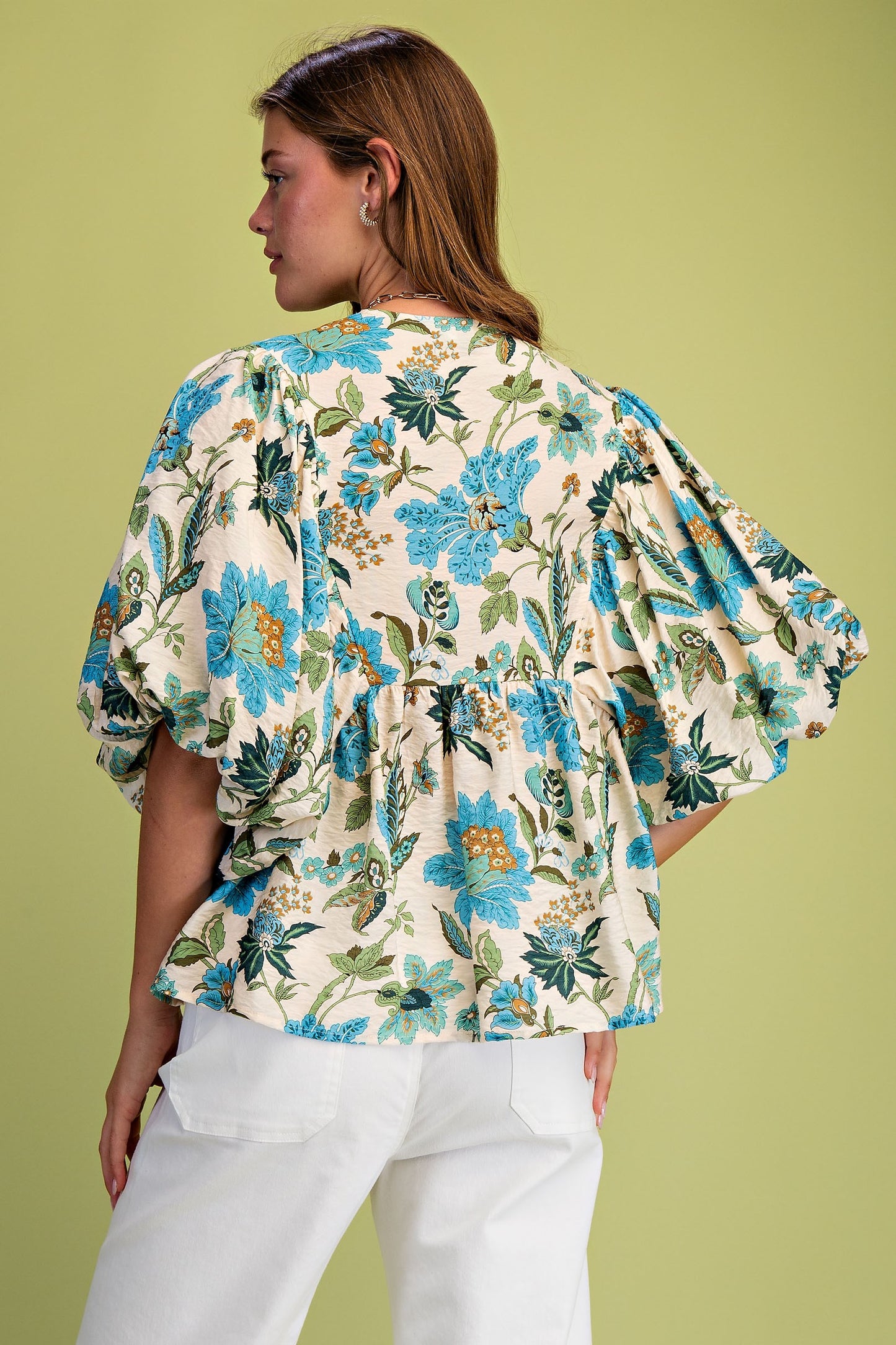 Woman wearing a floral blouse with white pants on a green background