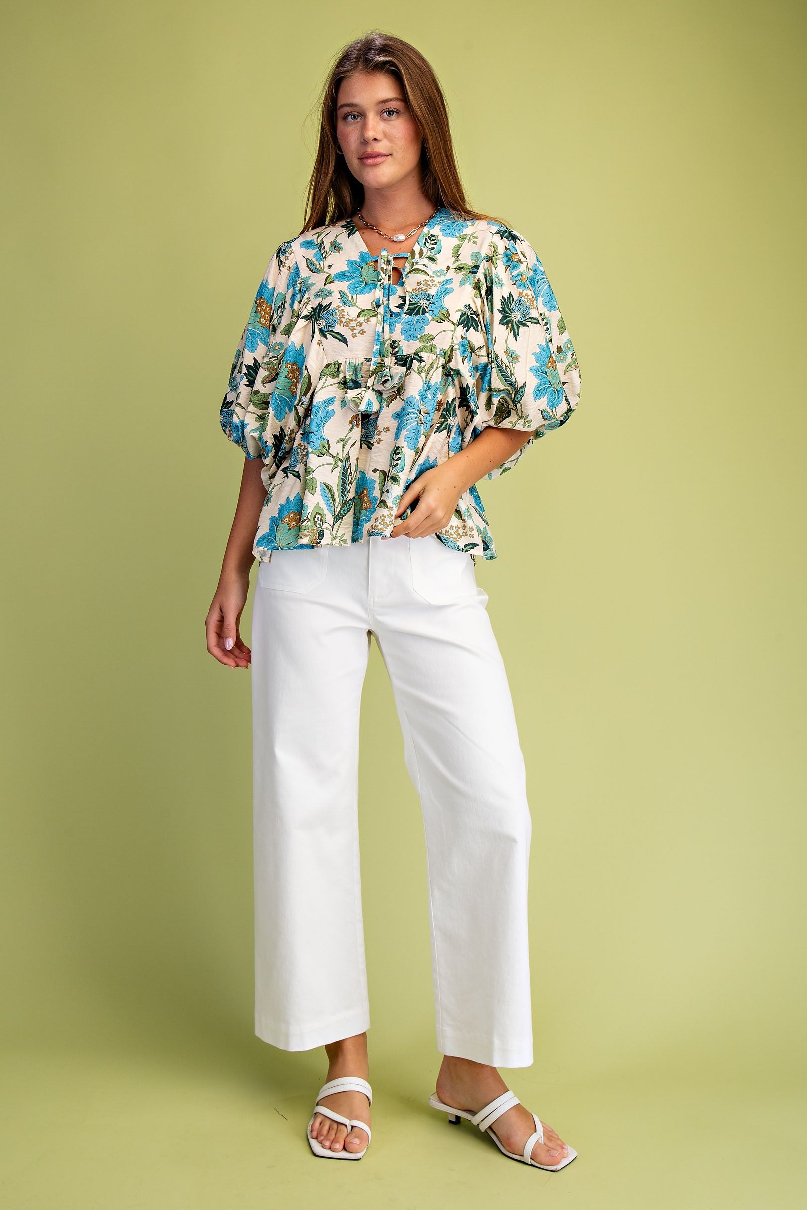 Woman wearing a floral blouse and white pants on a green background