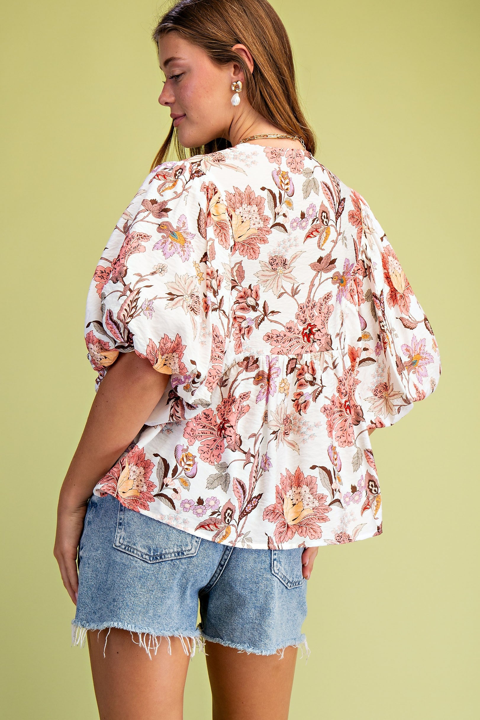 Woman wearing a floral blouse and denim shorts against a light green background