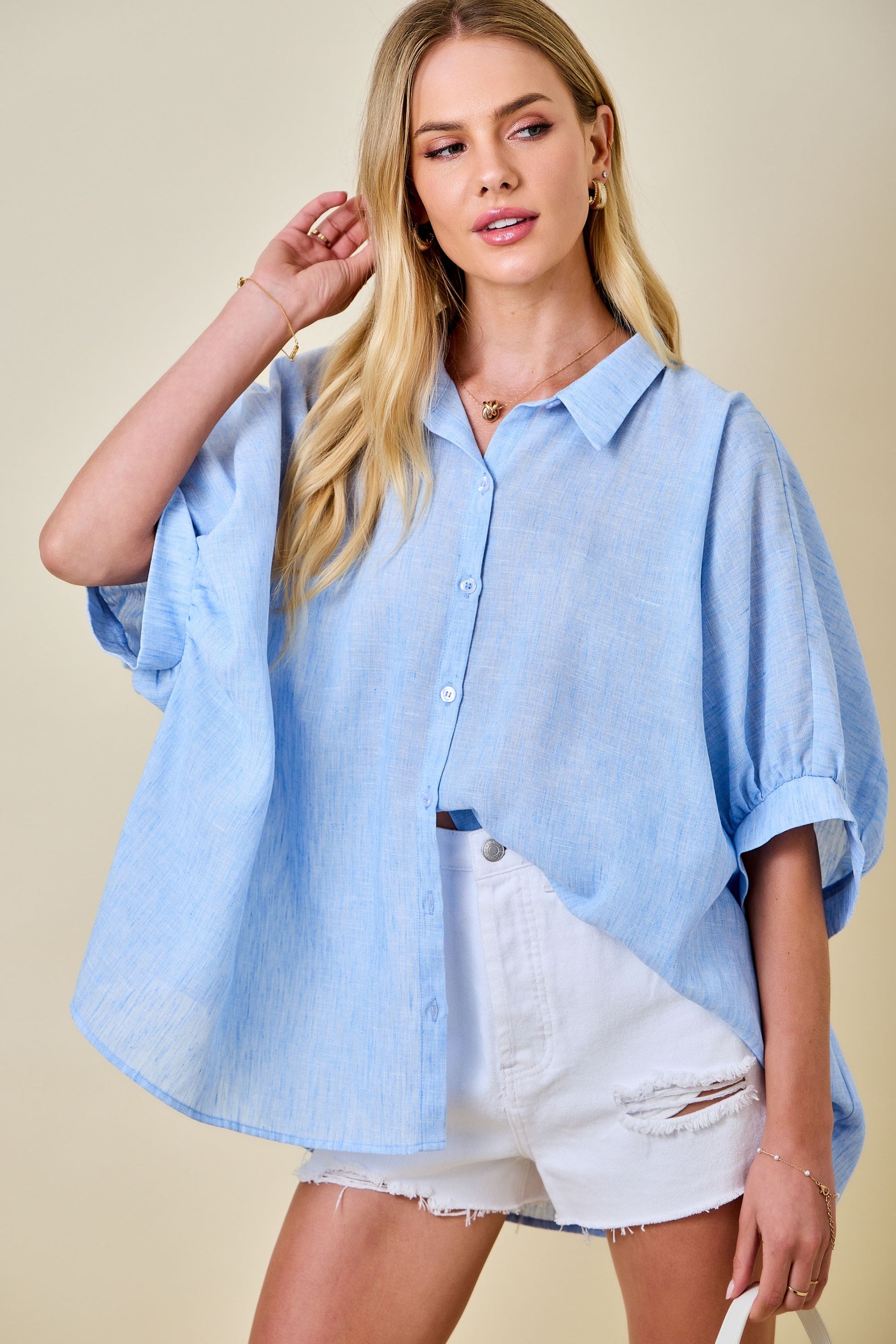 Woman wearing a light blue oversized shirt and white shorts on a beige background