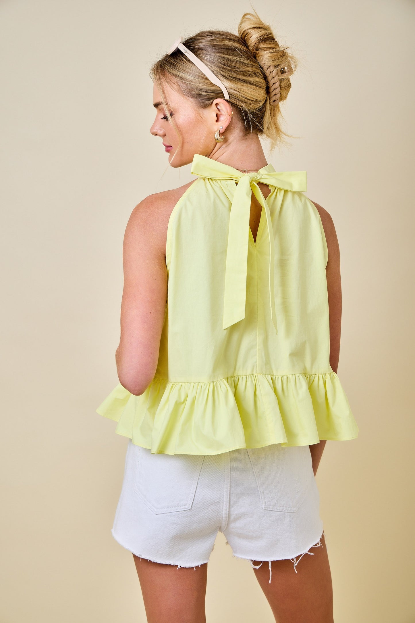 Woman wearing a yellow halter top with ruffled details and white shorts against a beige background