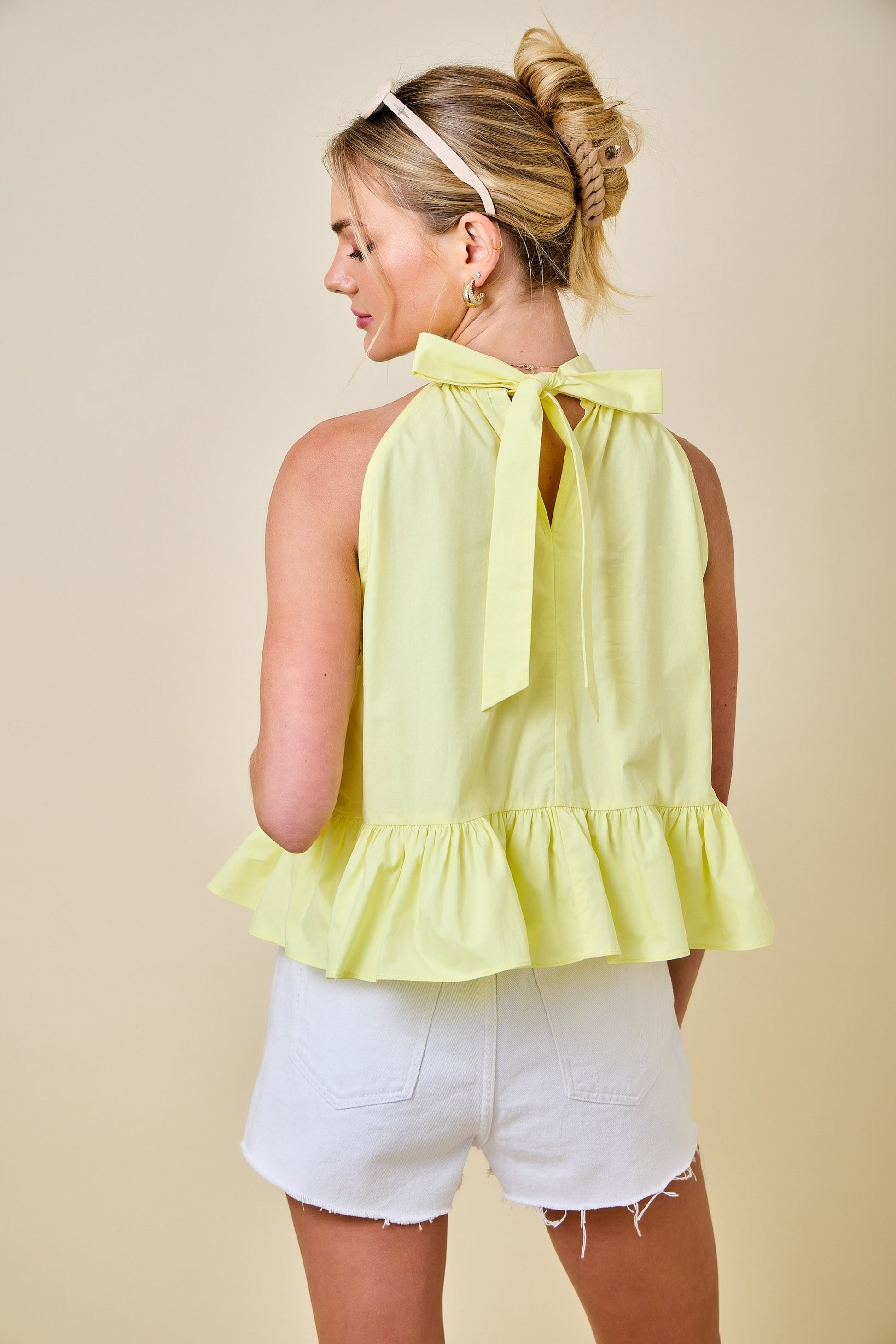 Woman wearing a yellow halter top with ruffled details and white shorts against a beige background