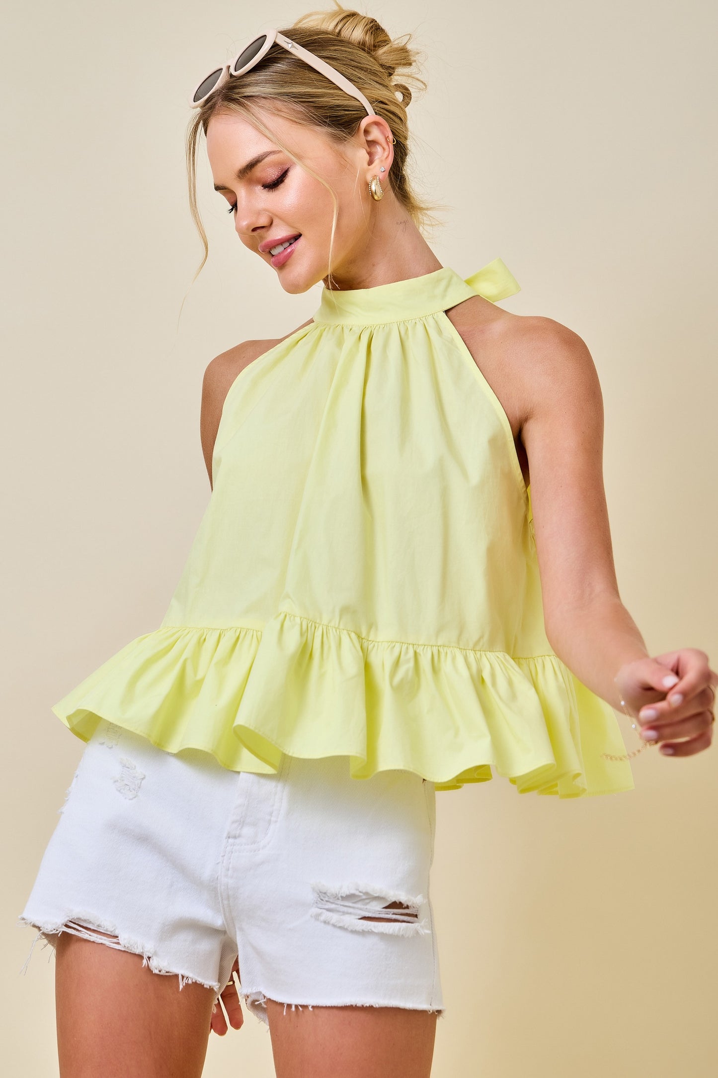 Woman wearing a yellow ruffled top and white shorts against a beige background
