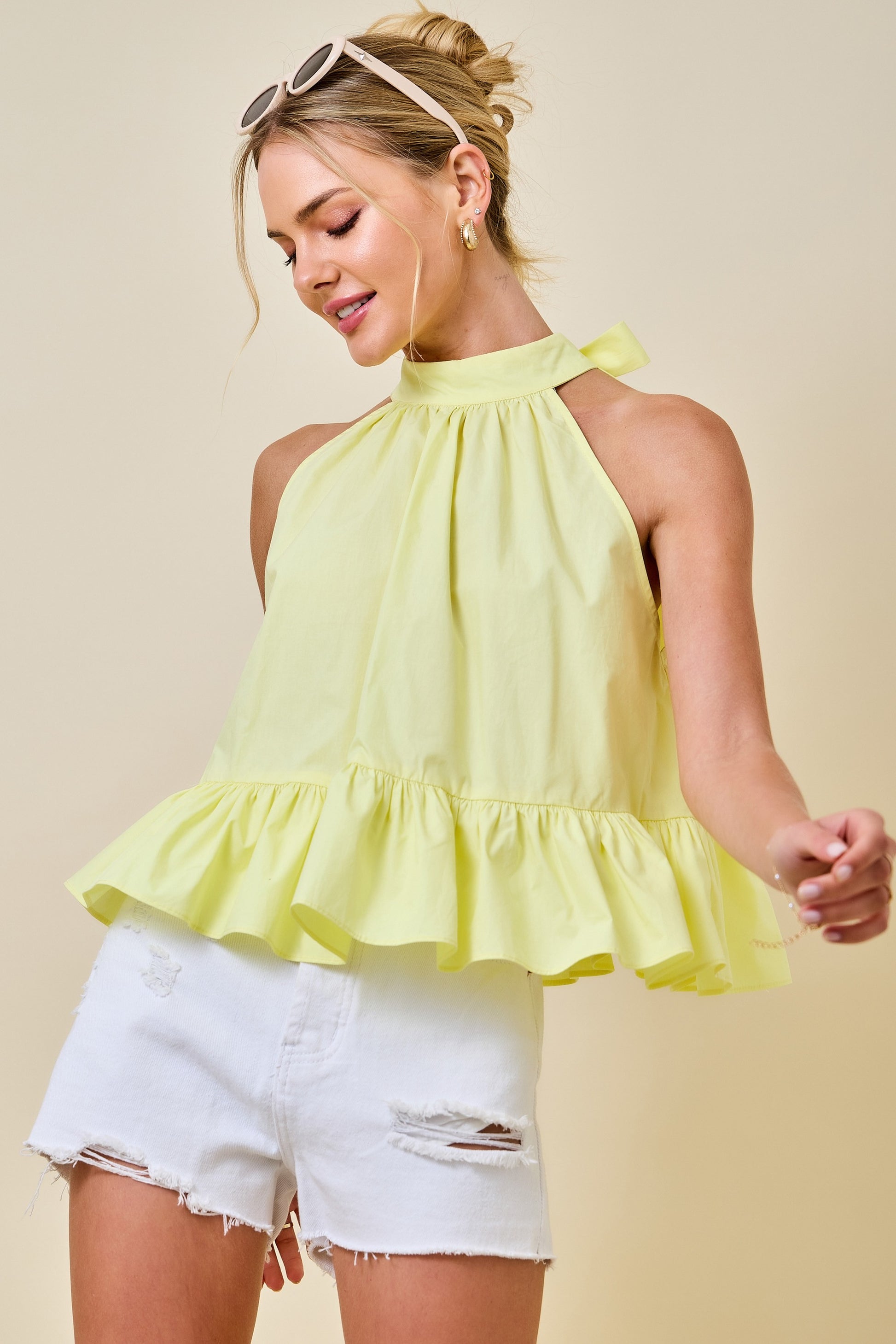 Woman wearing a yellow ruffled top and white shorts against a beige background