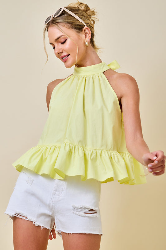 Woman wearing a yellow ruffled top and white shorts against a beige background
