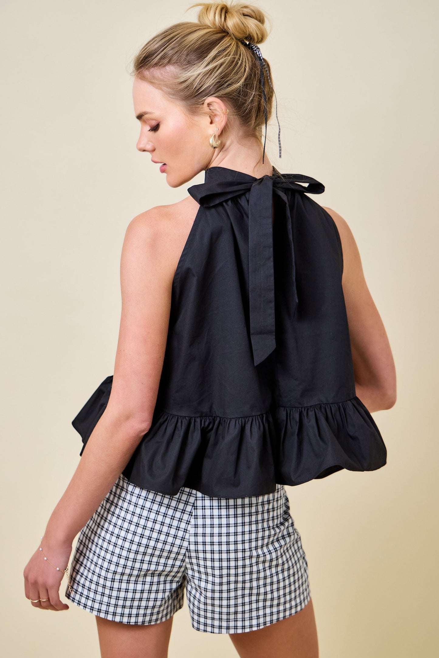 Woman wearing a black sleeveless top with a bow and checkered shorts on a beige background