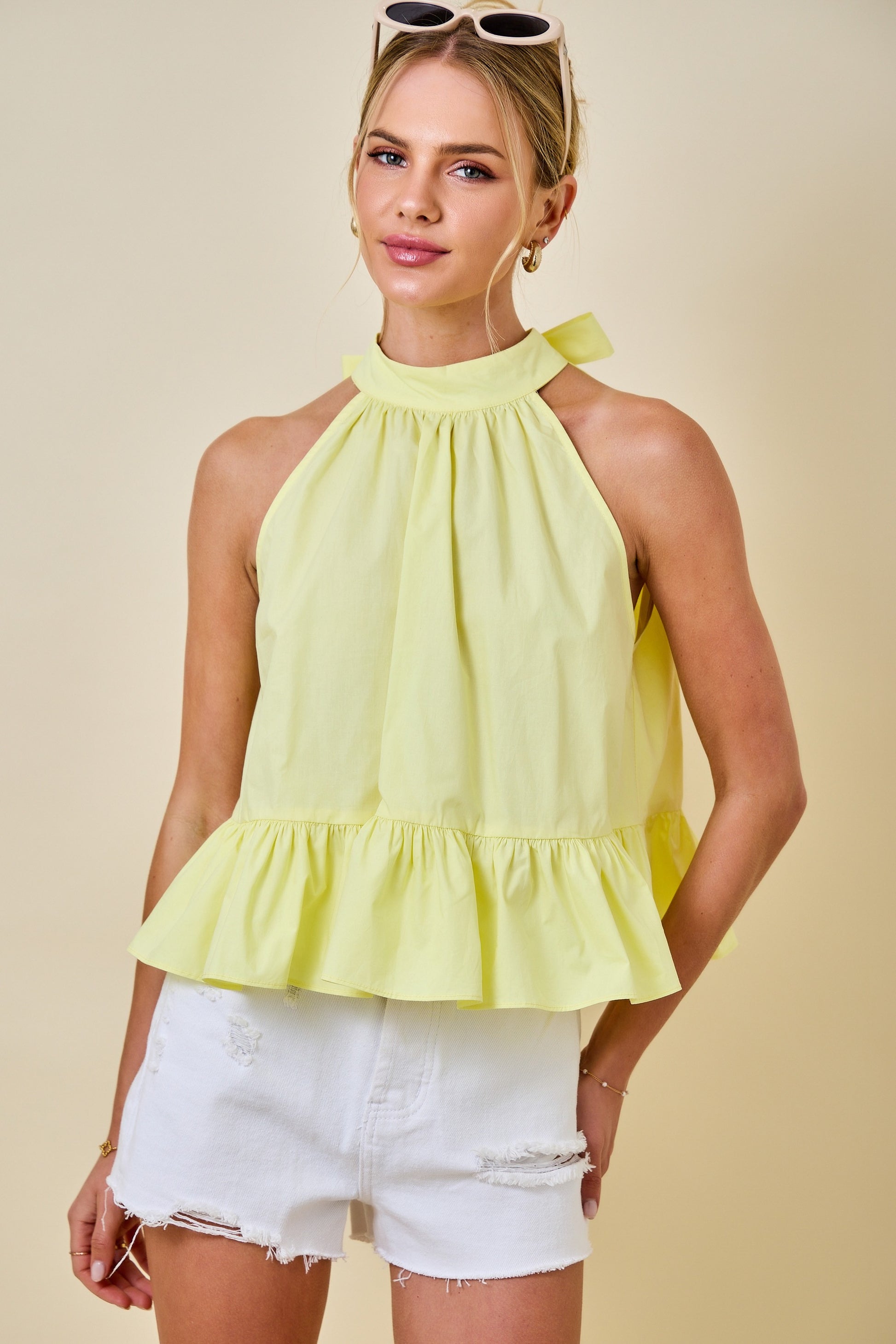 Woman wearing a yellow top and white shorts against a beige background