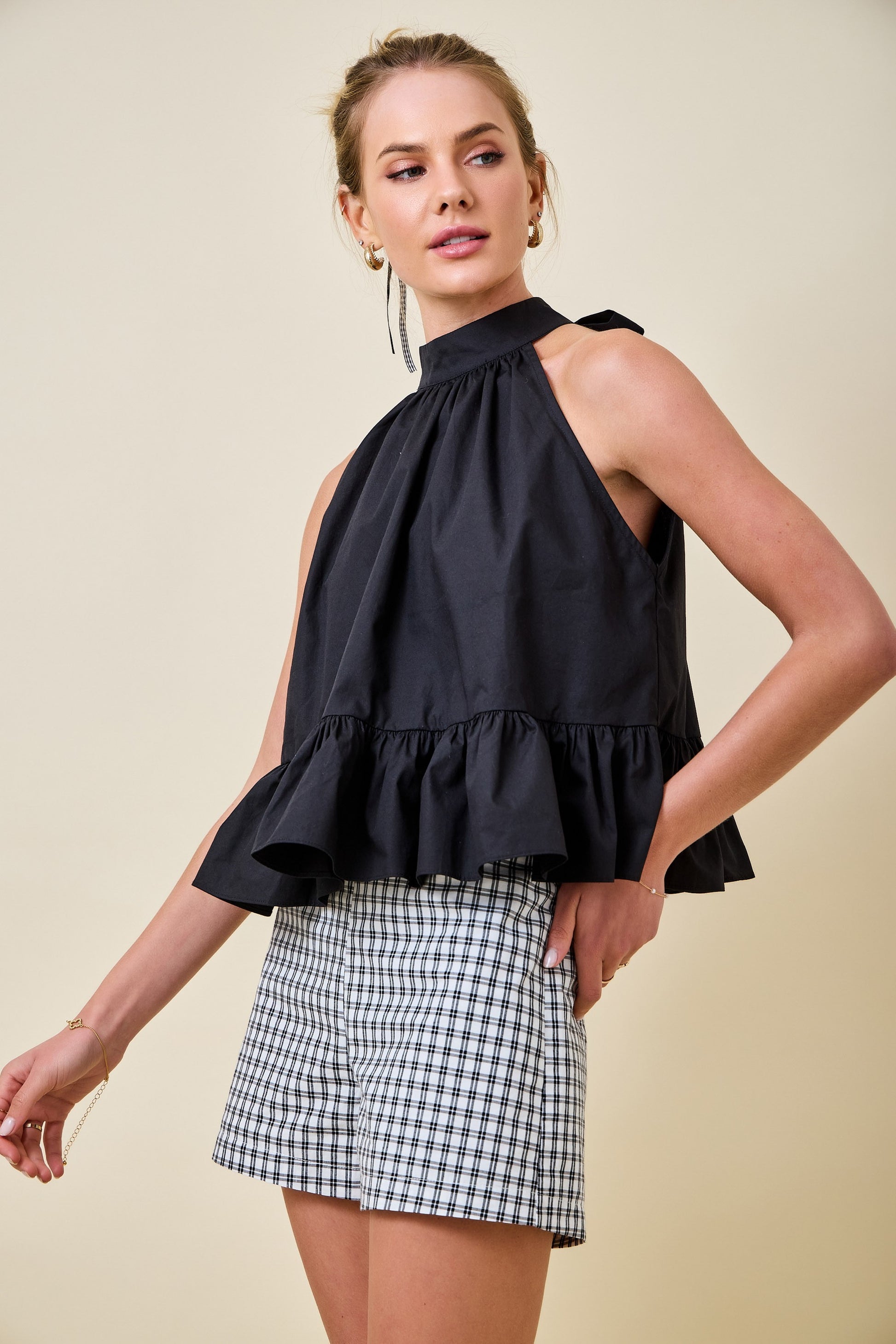 Woman wearing a black halter top with ruffled details and a plaid skirt on a beige background