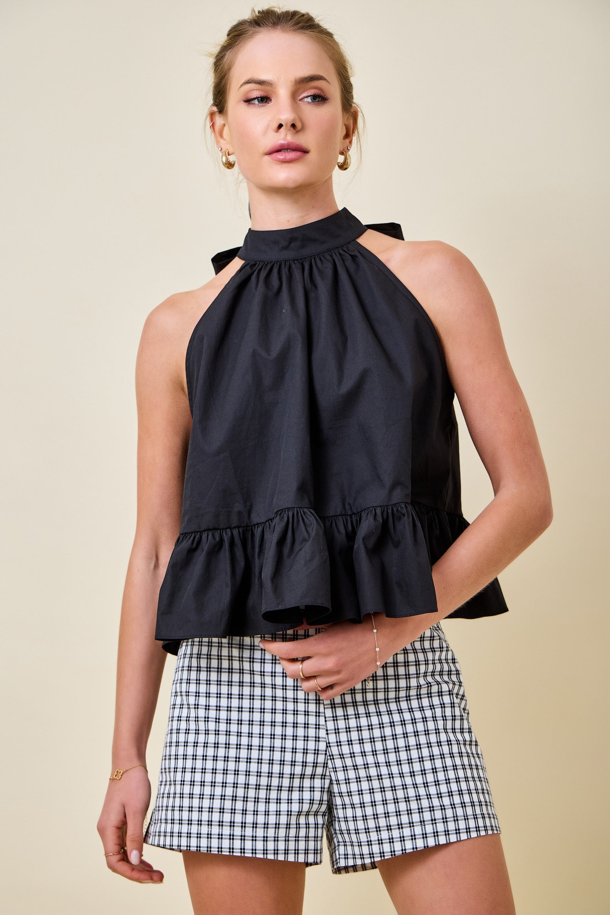 Woman wearing a black halter top and checkered shorts on a beige background
