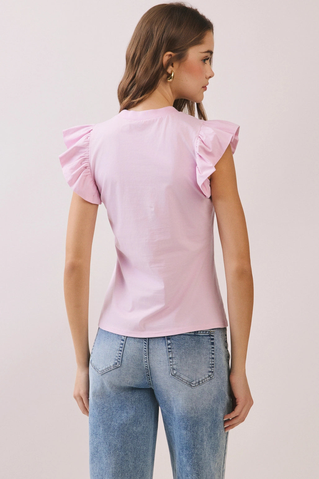 Woman wearing a pink top with ruffled sleeves and blue jeans on a light gray background