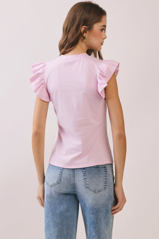 Woman wearing a pink top with ruffled sleeves and blue jeans on a light gray background
