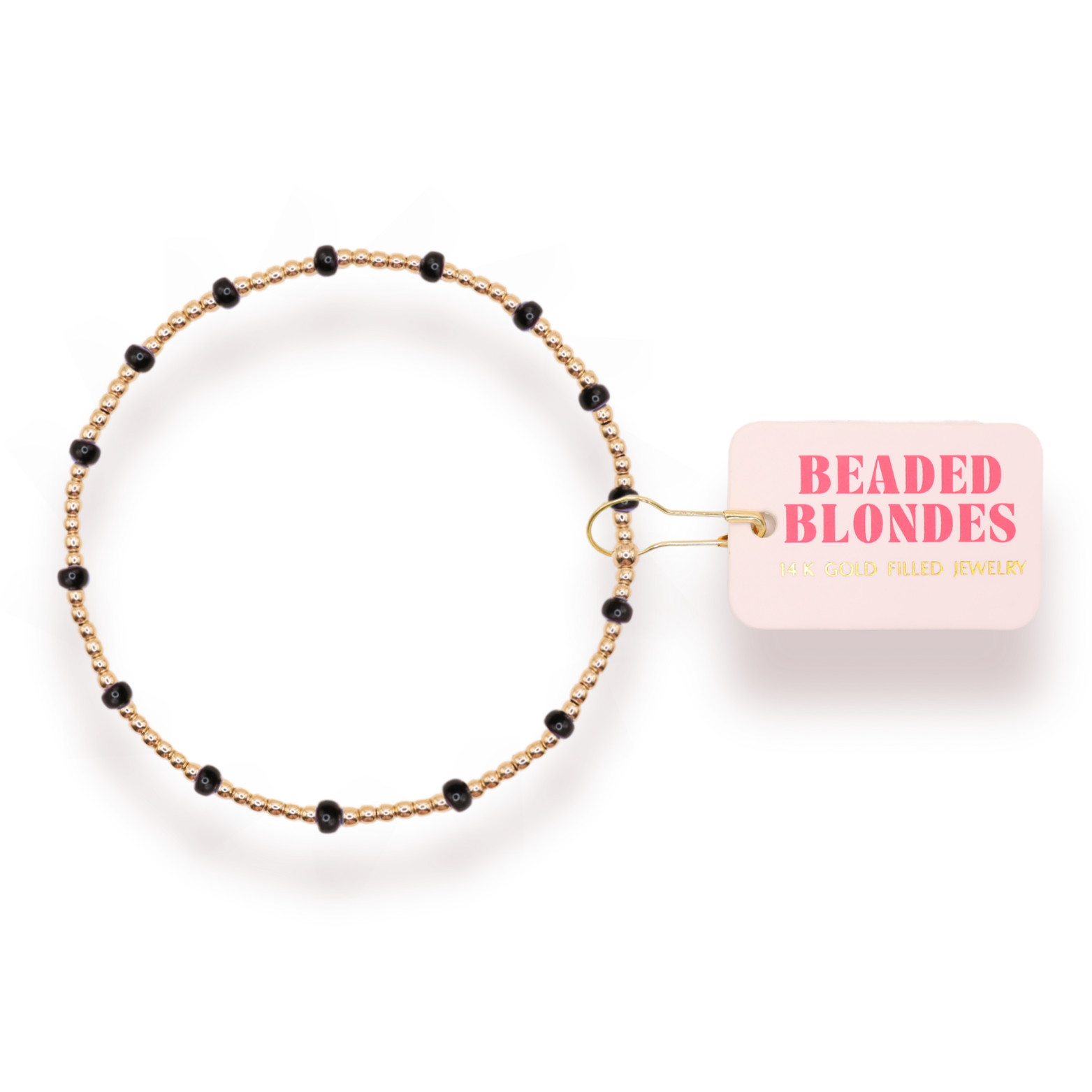A delicate beaded bracelet with a gold-toned twisted wire base and small black beads spaced along the band, shown next to a light pink paper tag that reads 'BEADED BLONDES'.