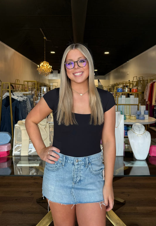 Woman wearing a black top and denim skirt in a store setting