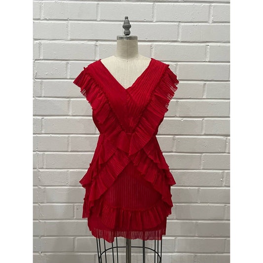 A bright red pleated ruffle dress displayed on a dress form mannequin against a white painted brick wall background.