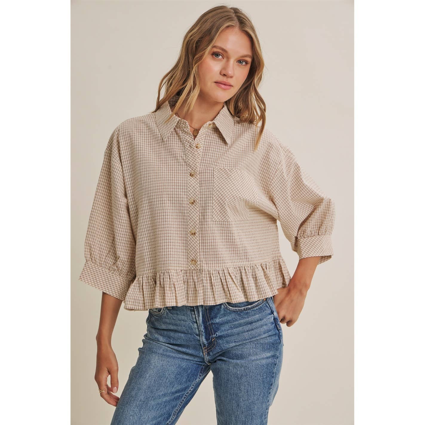 Woman wearing a checkered blouse and jeans against a neutral background