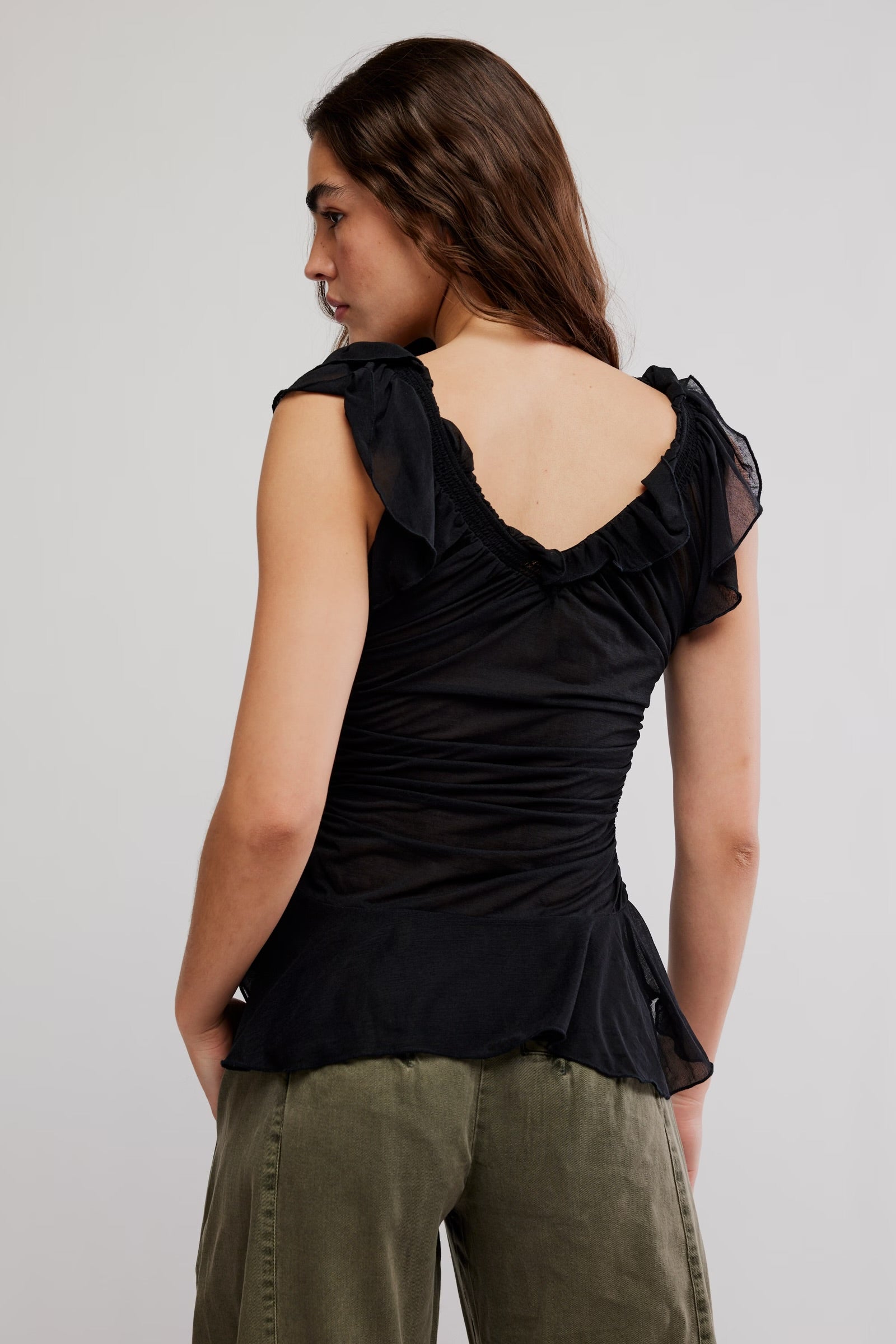 Model wearing black flowy tank top with green jeans facing backwards