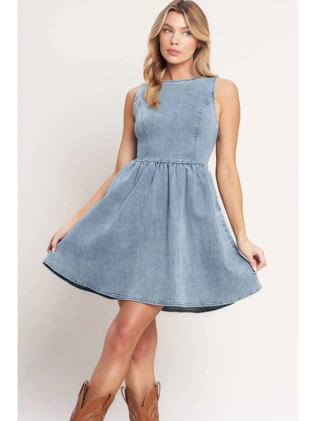 Woman wearing a light blue denim dress with brown boots on a white background