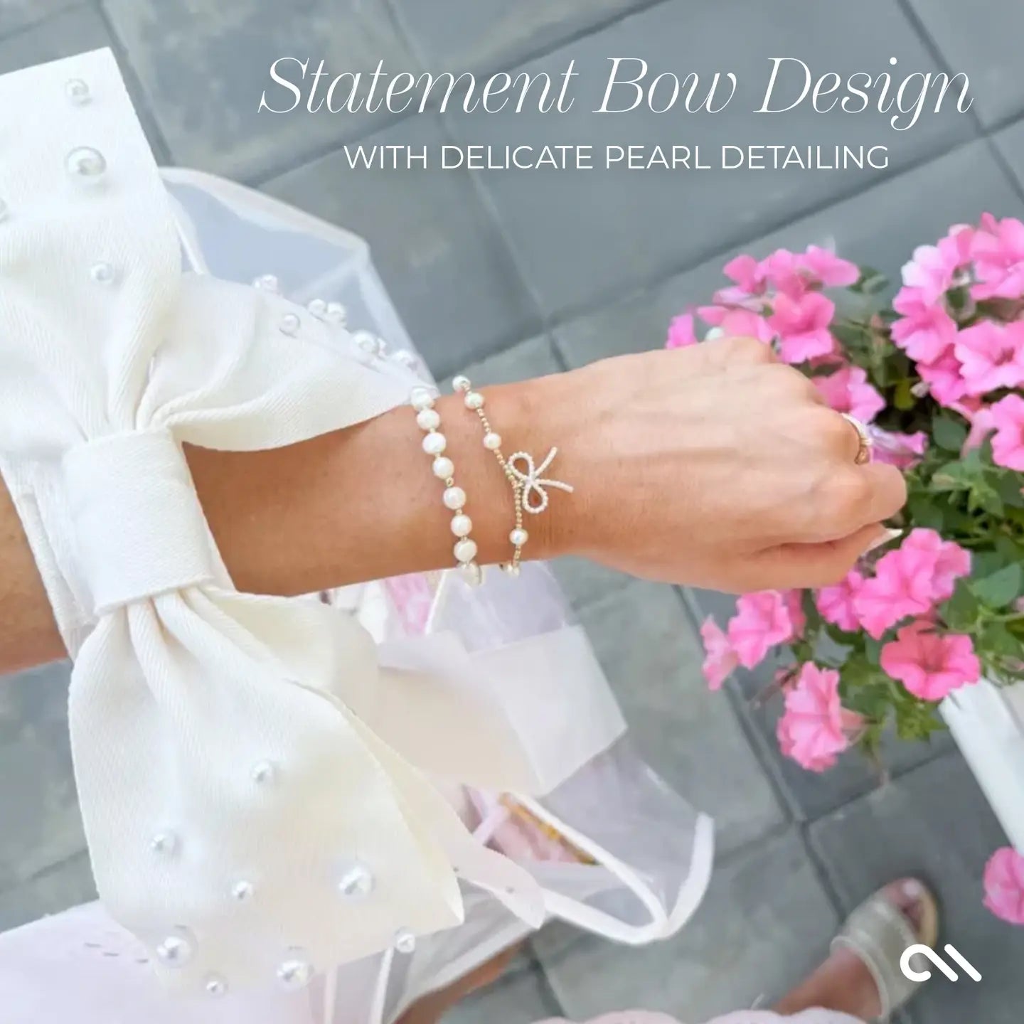 Pearl bracelet with bow design worn by a person holding pink flowers, on a blurred background.