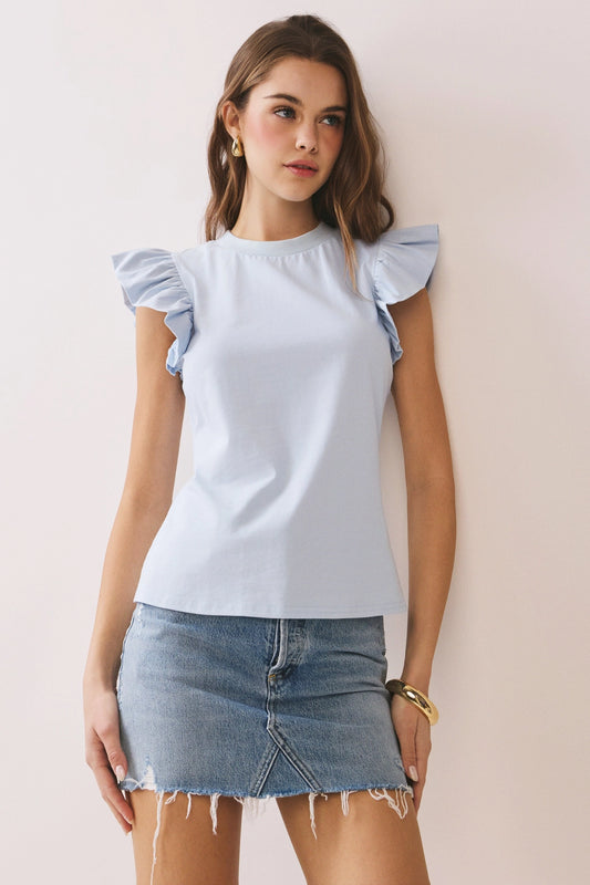 Woman wearing a light blue top with ruffled sleeves and a denim skirt against a plain background