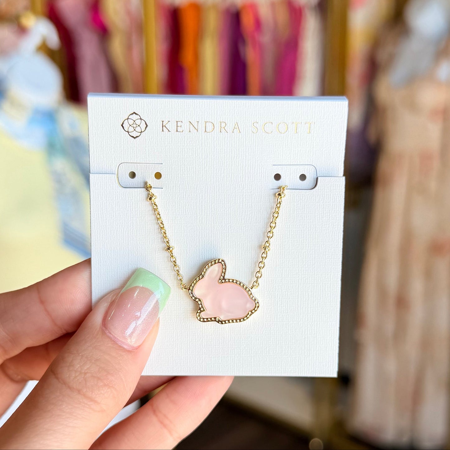 Hand holding a card with a necklace featuring a heart-shaped pendant against a blurred background