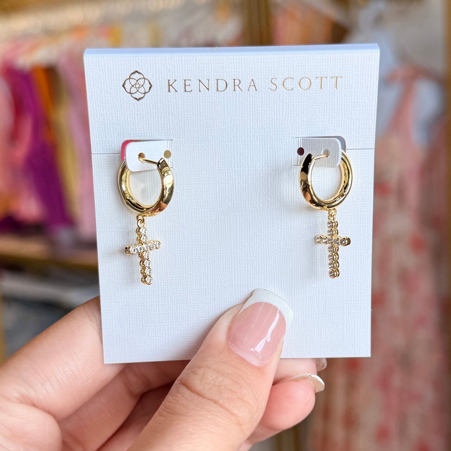Gold earrings on a Kendra Scott card held by a hand with a blurred background