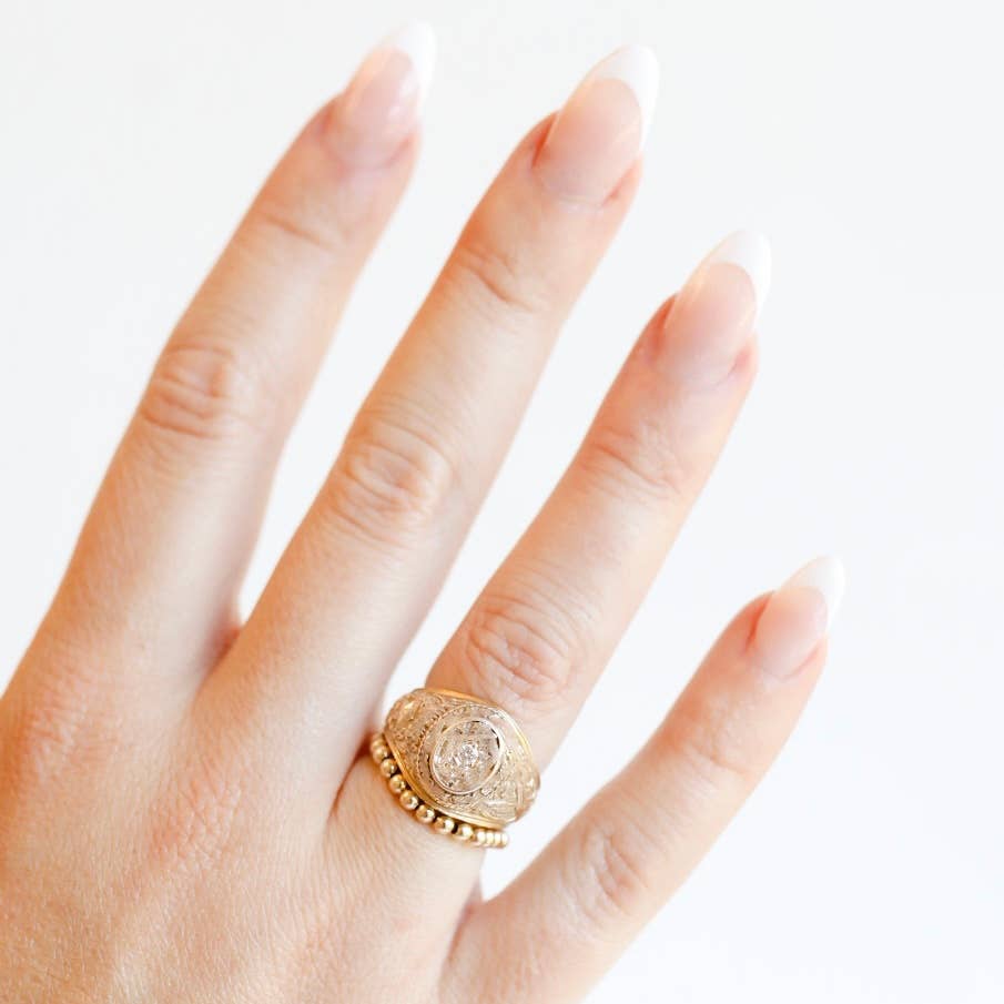 Gold ring with a decorative design on a person's finger against a white background