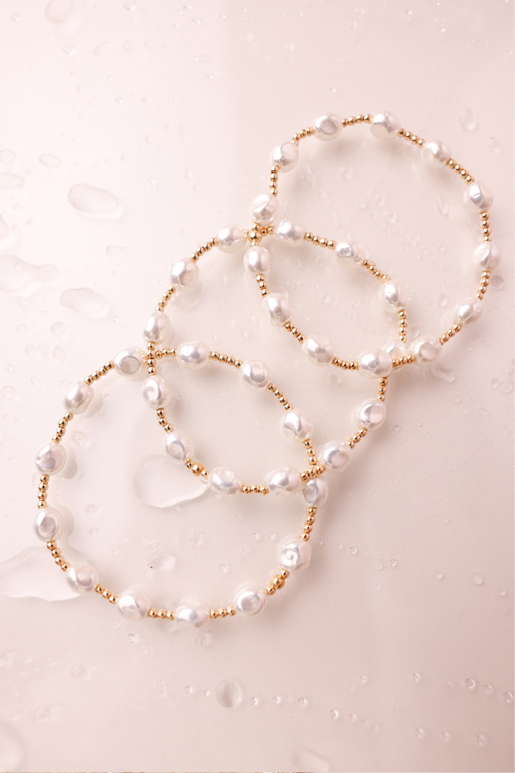 Two pearl necklaces with gold accents on a light pink textured background