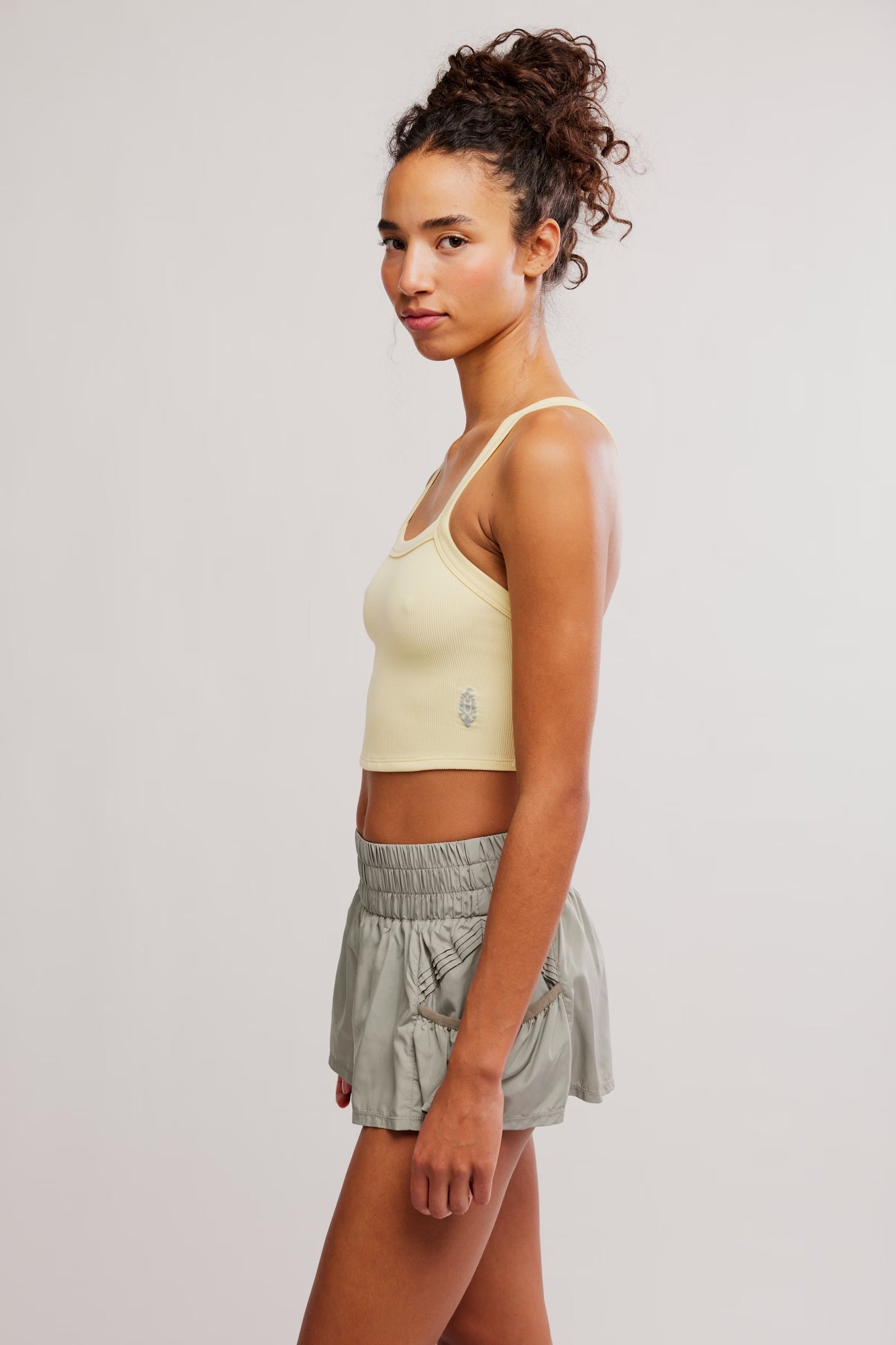 Woman wearing a light yellow sports bra and gray shorts on a plain background
