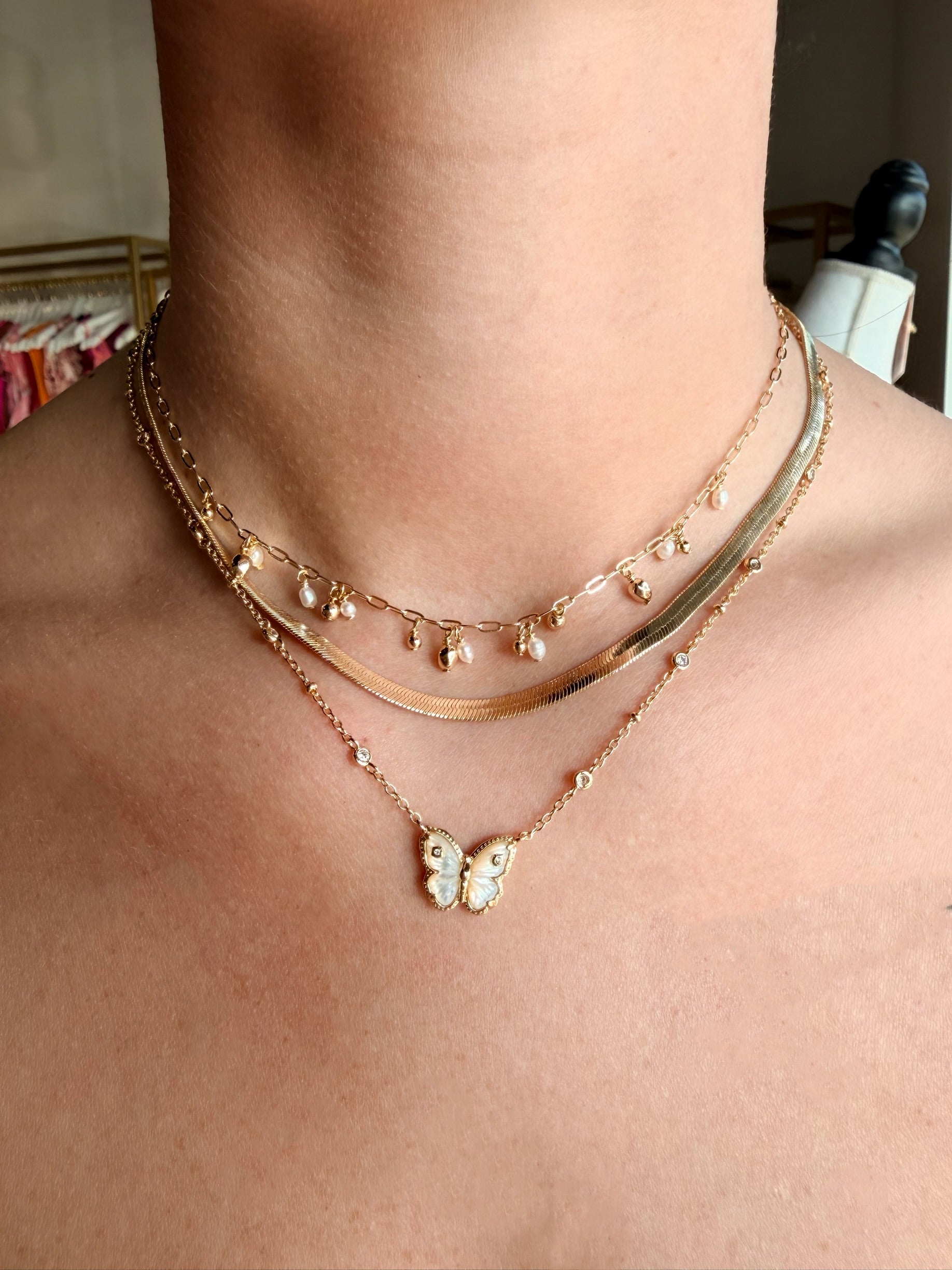 Two gold necklaces with butterfly pendants on a person's neck.