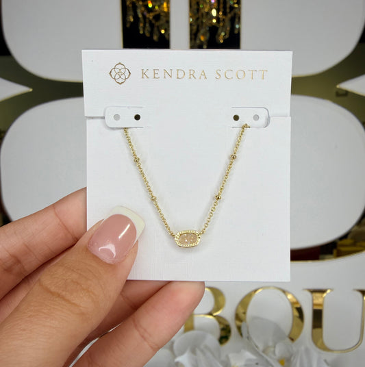 Gold necklace on a Kendra Scott card held by a hand with a blurred background