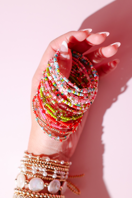 Hand wearing colorful beaded bracelets on a pink background