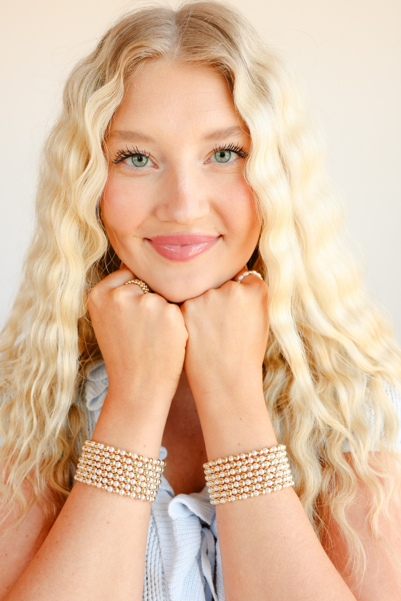 Woman with blonde hair wearing multiple gold bracelets on a plain background
