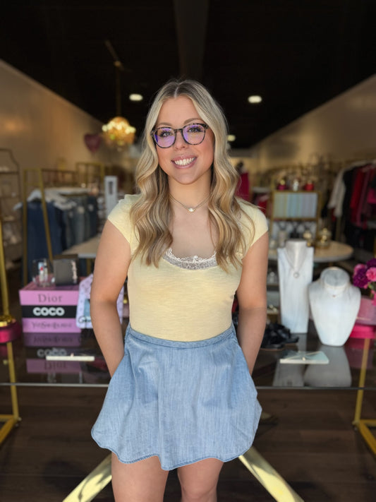 Person wearing a yellow top and denim skirt with a blurred background