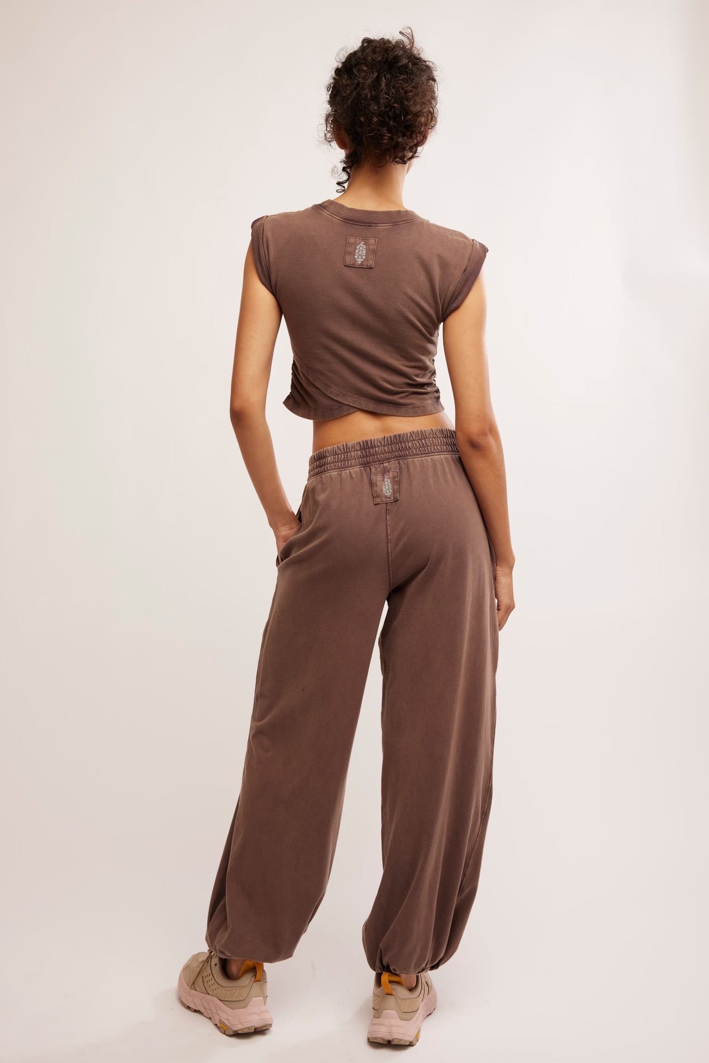 Person wearing a brown sleeveless top and wide-leg pants on a white background